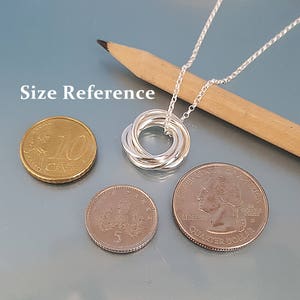 May include: Silver necklace with a five-ring knot pendant. The pendant is about the size of a US quarter. Size reference is shown with US coins.
