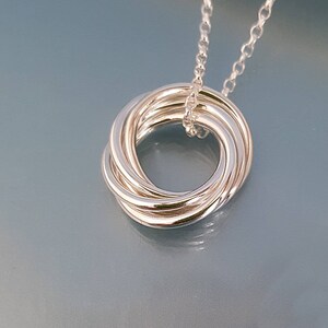 May include: A silver necklace with a pendant that is a circle made of multiple intertwined rings.