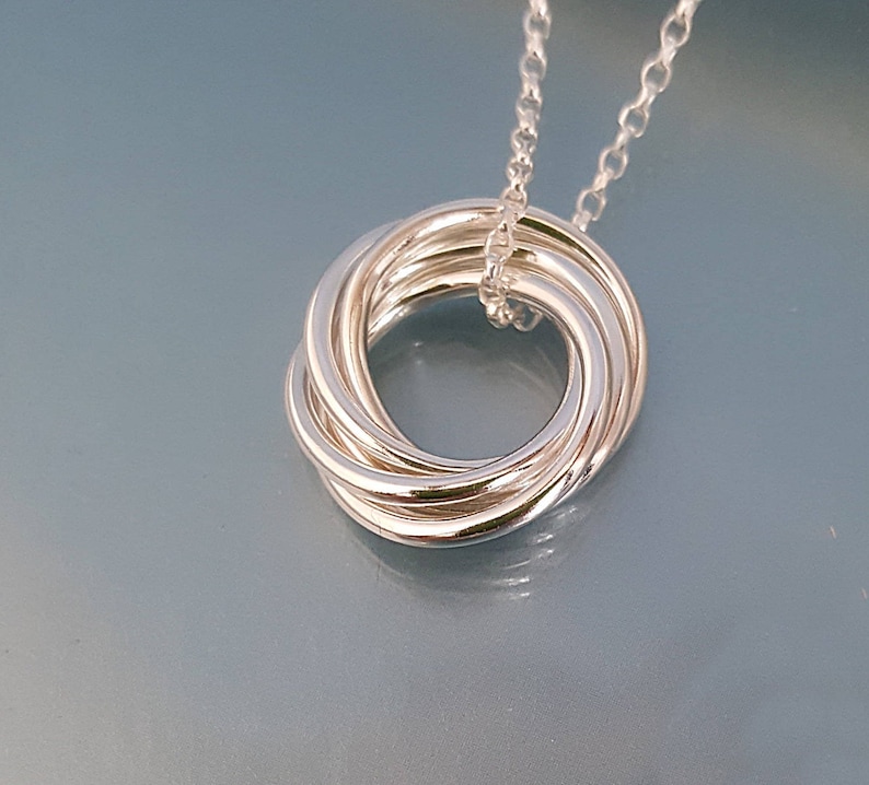 May include: A silver necklace with a pendant that is a circle made of multiple intertwined rings.