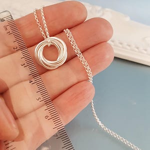 May include: A silver necklace with a circular pendant made of multiple intertwined rings. The necklace is 18 inches long.