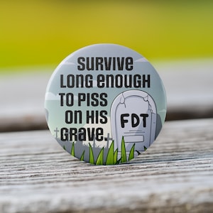 May include: A round button with a white background and black text that reads "Survive long enough to piss on his grave." A cartoon tombstone with the text "FDT" is in the background.