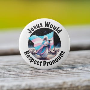 May include: A white button with the text "Jesus Would Respect Pronouns" in black. The button features a depiction of Jesus carrying a lamb, with a transgender pride flag in the background.