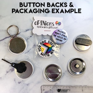 K&ouml;nnte beinhalten: Eine Auswahl an Knopf-R&uuml;ckseiten und Verpackungsbeispielen. Das Bild zeigt verschiedene Knopfdesigns, darunter einen Schl&uuml;sselanh&auml;nger, einen Magneten und Kn&ouml;pfe mit Anstecknadeln. Einige Kn&ouml;pfe haben Text wie "You are safe with me" und "Please don't call me miss or ma'am."