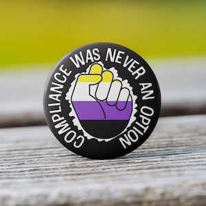 Puede incluir: Botón negro con el texto "Compliance was never an option" en blanco. Un puño estilizado con rayas amarillas, blancas, moradas y negras está en el centro.