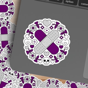 May include: A sticker featuring a purple and gray bandage design, surrounded by a wreath of flowers, hearts, and skulls. The bandage is the focal point, with a perforated center. The design is on a white background.