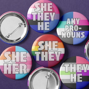 May include: A set of six round buttons with different pride flag designs and text. The buttons feature the text "She They He", "Any Pro-Nouns", "She They", "She Her", "They He", and a blank button.