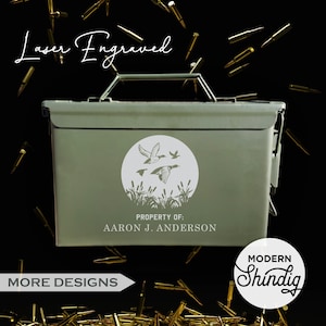 May include: Laser engraved, olive green metal ammo box with a white circular graphic of flying ducks over reeds. The text "PROPERTY OF: Aaron J. Anderson" is below the graphic. The box has a metal handle and clasp.