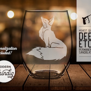 Puede incluir: Una copa de vino sin tallo con un diseño de zorro arenado. La copa presenta el texto "¡Personalización incluida!" y "Modern Shindig". La imagen también incluye el texto "Deep Etch de la más alta calidad, arenado permanentemente".