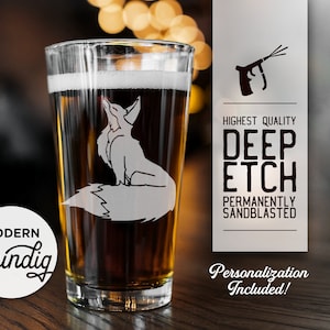 Puede incluir: Un vaso de pinta transparente con un diseño de zorro arenado, lleno de cerveza. El vaso tiene las palabras "Modern Shindig" en una etiqueta circular blanca. También es visible el texto "HIGHEST QUALITY DEEP ETCH PERMANENTLY SANDBLASTED".