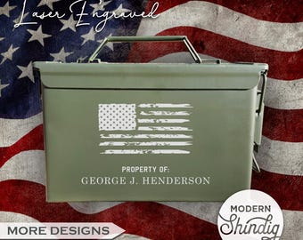 May include: A green metal box with a white distressed American flag design. The text "Laser Engraved" is at the top, and "PROPERTY OF: GEORGE J. HENDERSON" is below the flag. The background features an American flag.