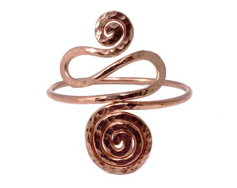 May include: Copper arm cuff with a hammered texture. The cuff features a spiral design at the top and bottom, connected by a curved band. The metal has a warm, reddish-brown hue, and the design is open and airy.