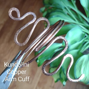 May include: A copper arm cuff with a hammered texture and a flowing, serpentine design. The cuff is being shaped with pliers. The text "Kundalini Copper Arm Cuff" is visible in the image.