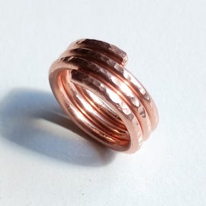 May include: A copper-colored ring with a hammered texture. The ring is made of multiple coils of metal, creating a layered effect. The design is simple yet eye-catching, suitable for everyday wear.