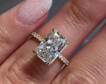 May include: A gold engagement ring with a large, rectangular, clear diamond. The diamond is set in a pave setting with smaller diamonds on the band.