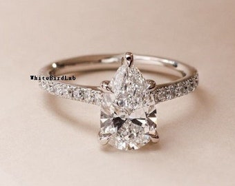 Puede incluir: Un anillo de compromiso de diamante de forma pera con una configuración de pavé en la banda. El anillo está engastado en oro blanco.