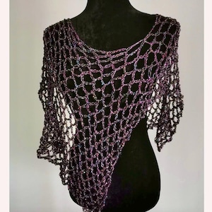 May include: A dark purple, open-weave shawl displayed on a black mannequin. The shawl has a net-like pattern with iridescent threads woven throughout, creating a shimmering effect. The garment drapes over the shoulders and has a pointed asymmetrical hemline.