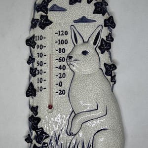 May include: A white ceramic thermometer shaped like a rabbit with blue ivy vines and clouds. The thermometer has a temperature scale from -20 to 120 degrees Fahrenheit.
