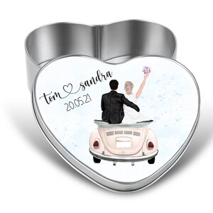 Könnte beinhalten: Herzförmige Metallbox mit Deckel mit Hochzeitsillustration. Der Deckel zeigt ein Paar in einem Oldtimer, mit den Namen "Tom & sandra" und dem Datum "20.05.21" in Schrift. Die Dose ist silberfarben.