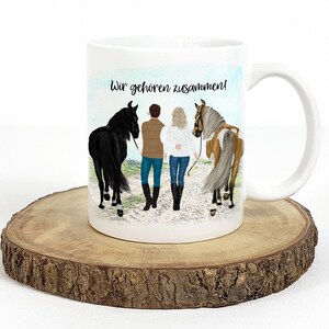May include: White ceramic mug with a colorful illustration of a couple walking with their horses. The text "Wir geh&ouml;ren zusammen!" is printed on the mug.