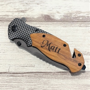 Peut inclure: Un couteau de poche avec un manche en bois et une lame à motif en fibre de carbone. Le manche est gravé du nom "Matt".