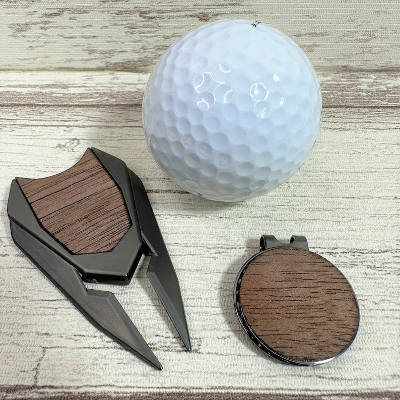 Pu&ograve; includere: Un set di tre accessori per il golf: una palla da golf, un marcatore per palla da golf e un raccoglitore di palle da golf. La palla da golf &egrave; bianca con le fossette. Il marcatore per palla da golf &egrave; un disco rotondo marrone con un bordo metallico. Il raccoglitore di palle da golf &egrave; uno strumento in metallo nero con un manico in legno.