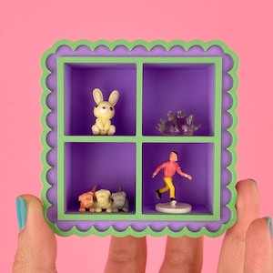May include: A miniature purple and green shelf with four compartments, each holding a small figurine. The figurines include a yellow bunny, a clear crystal, a running figure, and three small dog figurines. The background is pink.