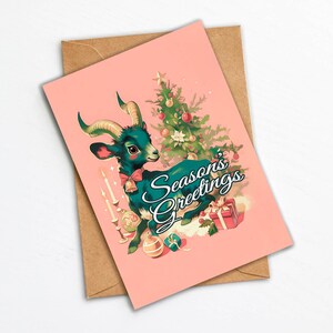 May include: A pink Christmas card with a green goat wearing a red bow and a Christmas tree in the background. The text on the card reads "Seasons Greetings".