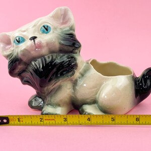 May include: A vintage ceramic cat planter with blue eyes, black and gray fur, and a pink nose. The planter is approximately 7 inches long. The cat is in a seated position with a hollowed-out back for plants.
