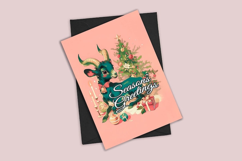 May include: A pink Christmas card with a green goat wearing a red bow and bells. The goat is sitting under a Christmas tree with ornaments and candles. The text "Seasons Greetings" is written in black cursive.