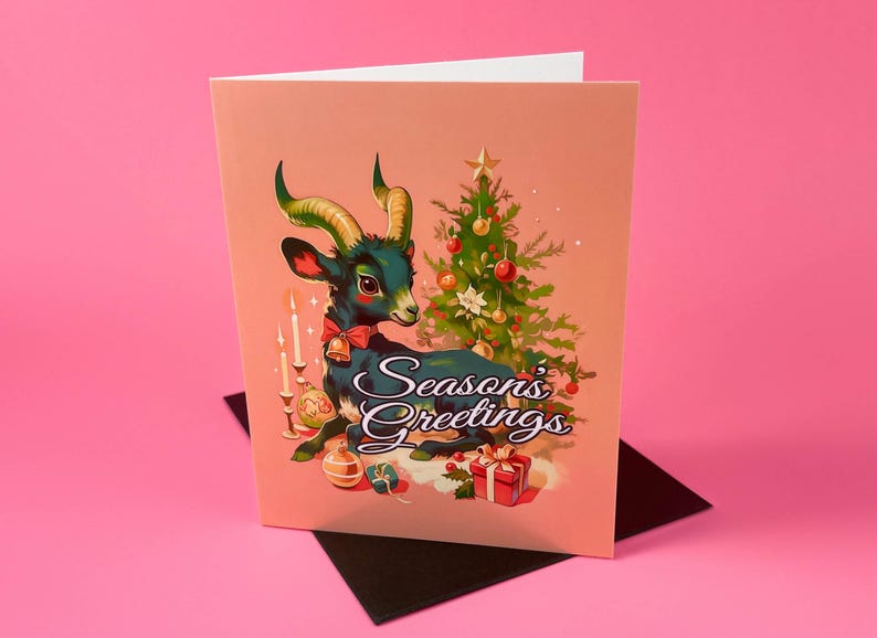May include: A Christmas card featuring a blue and green goat with a red bow, sitting in front of a decorated Christmas tree. The card has a pink background and the text "Season's Greetings".