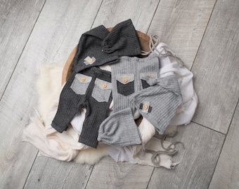 Könnte beinhalten: Zwei Sets Neugeborenenkleidung in Grau und Dunkelgrau. Jedes Set enthält ein Kapuzenoberteil und eine Hose mit einer aufgesetzten Tasche. Die Kleidung ist aus einem weichen, gerippten Stoff.