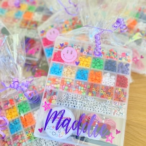 May include: A clear plastic container filled with colorful beads, letter beads, and string. The container is labeled "Maddie".
