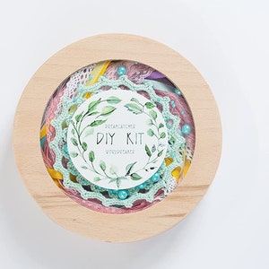 May include: A wooden round box with a clear lid containing a DIY dreamcatcher kit. The kit includes a variety of materials, including lace, ribbon, beads, and a small card that says "Dreamcatcher DIY Kit".