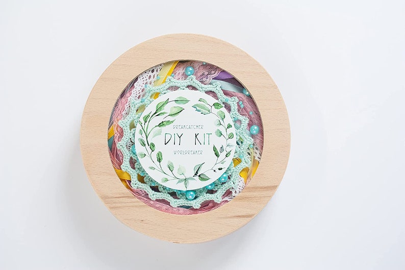 May include: A wooden round box with a clear lid containing a DIY dreamcatcher kit. The kit includes a variety of materials, including lace, ribbon, beads, and a small card that says "Dreamcatcher DIY Kit".