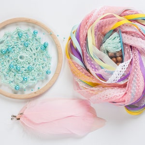 May include: A light blue crochet dreamcatcher with turquoise beads, pink feathers, and a pile of colorful ribbons and lace.