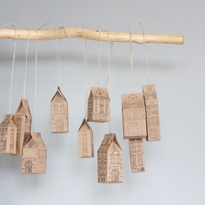 May include: A wooden branch with brown paper houses hanging from it with twine. The houses are decorated with a black and white print of a building.