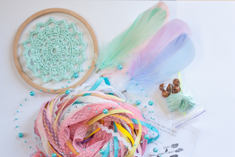 May include: A dream catcher kit with a light green crocheted circle, pastel feathers, pink and yellow ribbons, turquoise beads, and brown wooden beads.