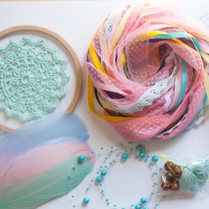 May include: A DIY dreamcatcher kit with a wooden hoop, light blue crochet lace, pink and blue feathers, turquoise beads, pink and yellow ribbon, and a small bag of turquoise yarn.