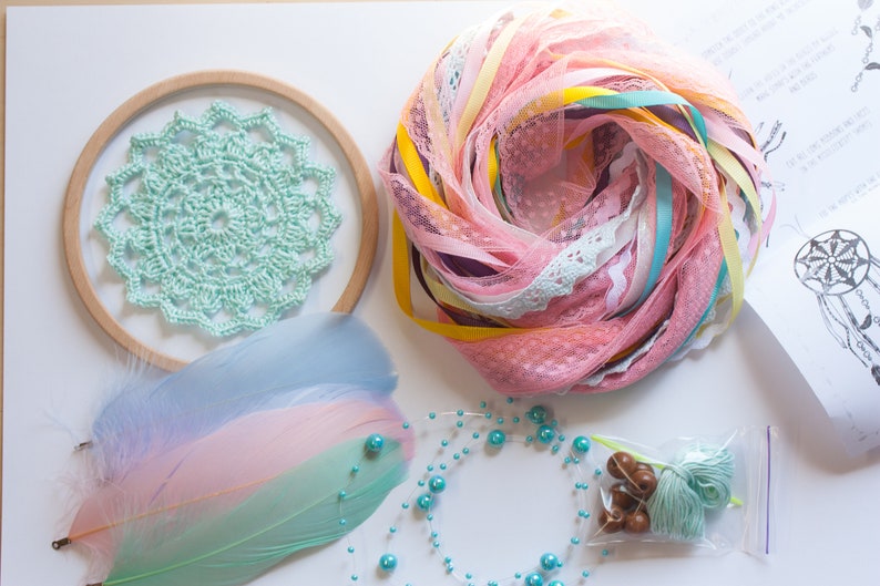 May include: A DIY dreamcatcher kit with a wooden hoop, light blue crochet lace, pink and blue feathers, turquoise beads, pink and yellow ribbon, and a small bag of turquoise yarn.