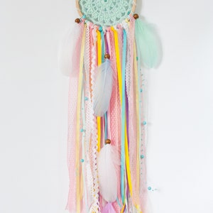 May include: A pastel-colored dream catcher with a green crocheted circle, white, pink, and yellow feathers, and various ribbons hanging from the bottom.
