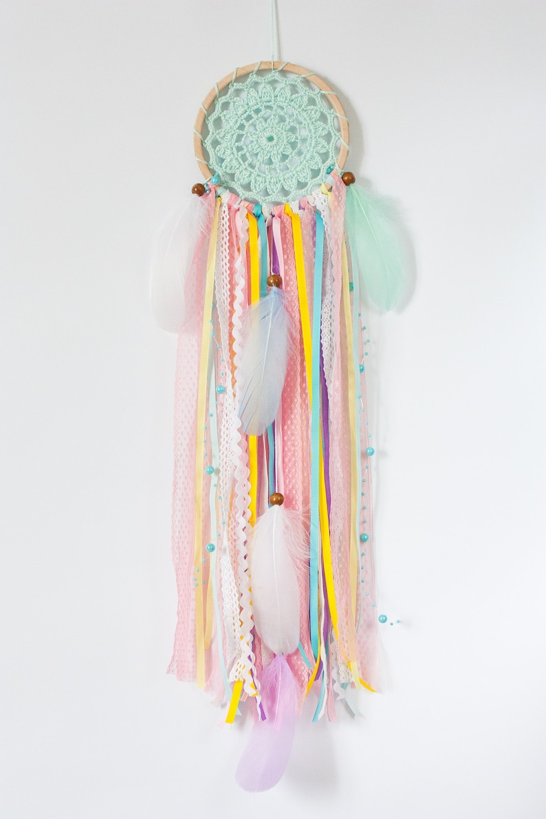 May include: A pastel-colored dream catcher with a green crocheted circle, white, pink, and yellow feathers, and various ribbons hanging from the bottom.