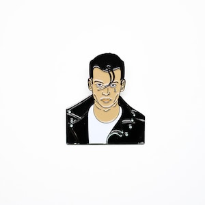 May include: Black and white enamel pin of a man with a black leather jacket, a white t-shirt, and a tear running down his cheek.
