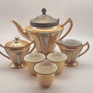 May include: A vintage tea set with a gold and white geometric design. The set includes a teapot, creamer, sugar bowl, and three cups.