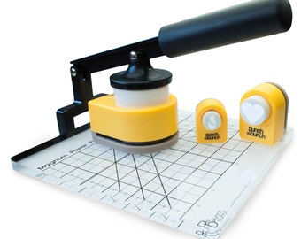 May include: A yellow and black punch tool with a clear plastic cutting mat. The tool has a handle and a base with a round punch. There are two smaller punches, one with a pineapple design and the other with a heart design. The mat has a grid pattern and the text "Magnum Power Punch" and "Punch Bunch" printed on it.