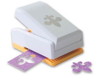 May include: A white paper punch with a yellow base. The punch is designed to cut out a fleur-de-lis shape. A purple glitter paper is being punched and a purple glitter fleur-de-lis has been punched out.
