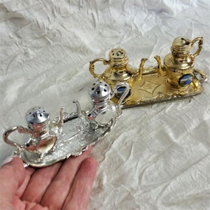 May include: Set of three silver and gold teapot salt and pepper shakers on a silver tray. The shakers have a vintage look and are perfect for adding a touch of whimsy to your kitchen.