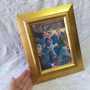 May include: A framed vintage print with a gold-coloured, textured frame. The artwork shows a group of smartly dressed people in a social setting, with a central gathering. The colour palette includes blues, purples, and neutral tones.