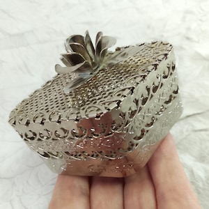 May include: Silver metal trinket box with a floral design and a flower on the lid.