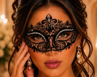 May include: A black filigree masquerade mask featuring intricate scrollwork patterns and embedded clear crystals along the eye openings. The mask covers the upper face and is paired with gold-toned drop earrings featuring white pearls.