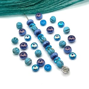May include: A collection of loose round beads in shades of metallic blue, purple, and teal, featuring both smooth and ribbed textures. A single metal wire holds a vertical row of these beads, which terminates in a small spiral loop at the end.